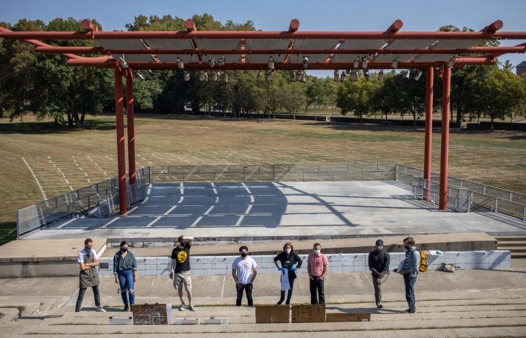 A class looks at paintings set up at a park amphitheater