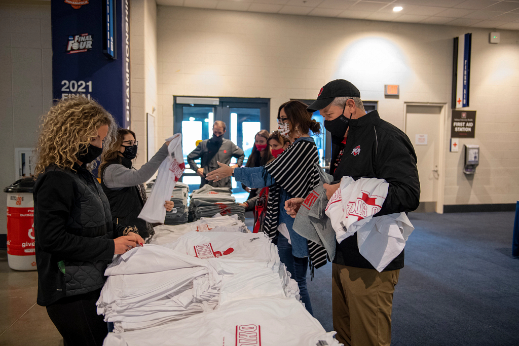 people with masks standing around tables with t-shirts