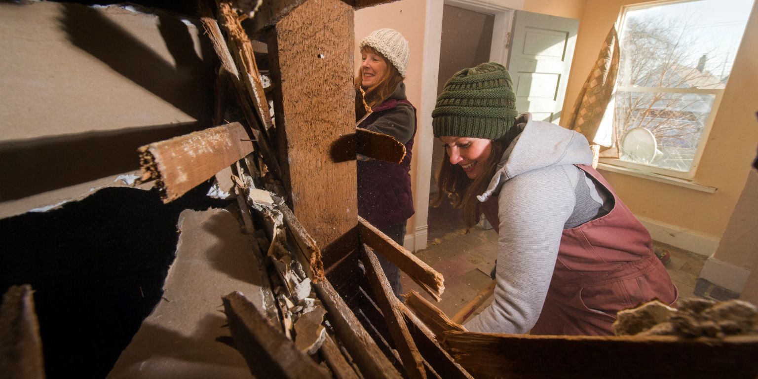 Mina and Karen work to tear down a wall in a house they are renovating.