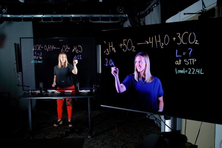 A woman writes math problems on a clear screen