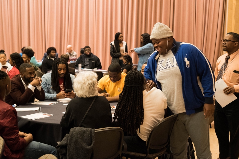 2018 Black History Month event participants visit with each other at round tables, some standing