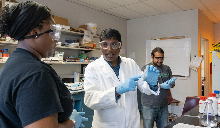 Rajesh Sardar, center, and two others work in a lab, all wearing goggles and gloves