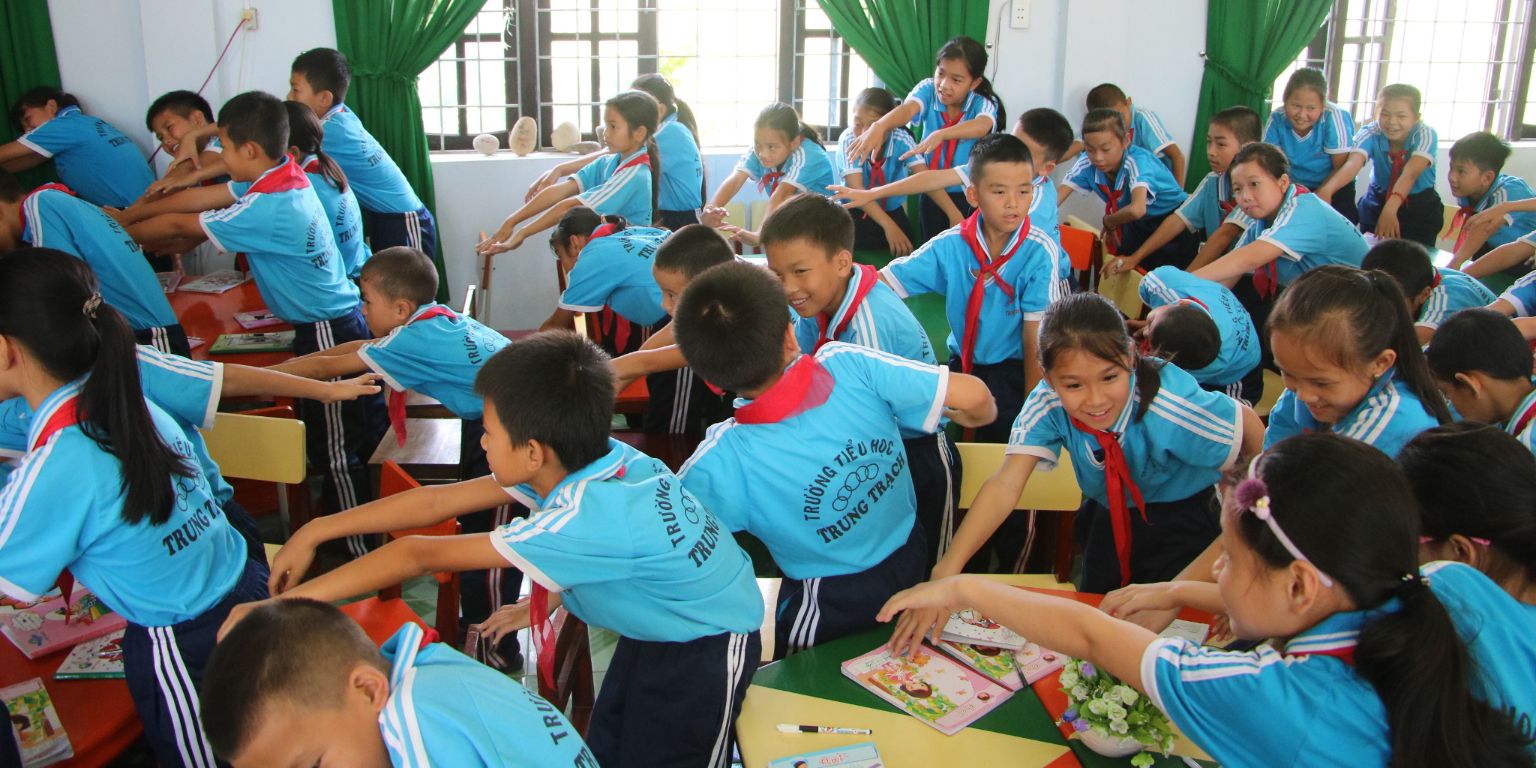 Children in Vietnam perform water safety exercises in a classroom.