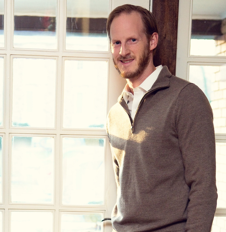 Matt Kent stands in front of a window, smiling.