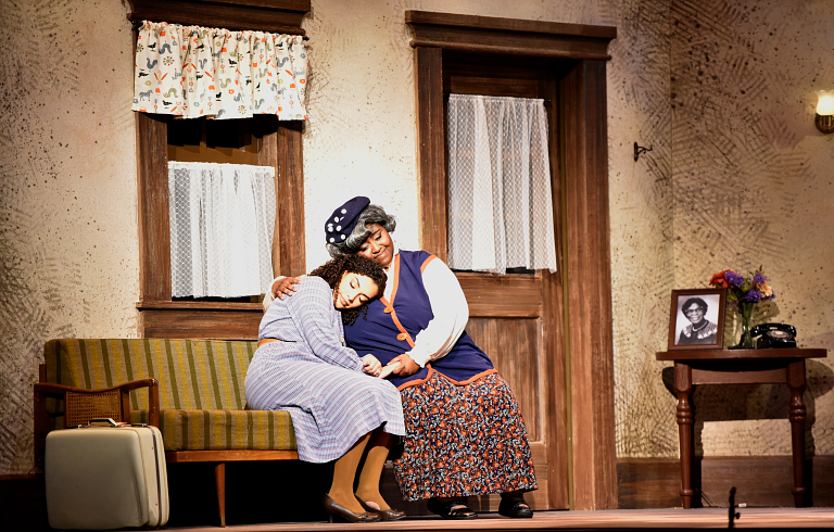 A female performer hugs another female performer onstage during their performance.