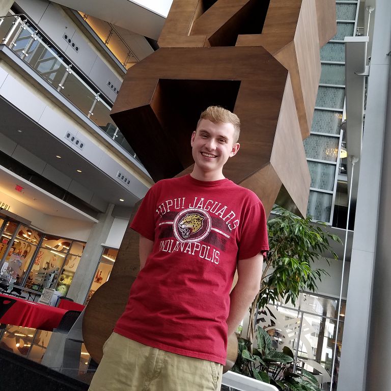 Michael Stottlemeyer stands in front of a wooden sculpture, smiling down at the camera.