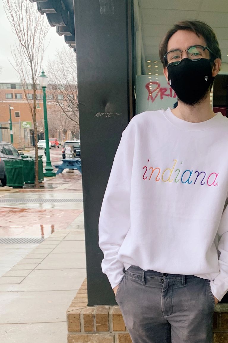 Student stands outside Tracks wearing a white sweatshirt with a rainbow 