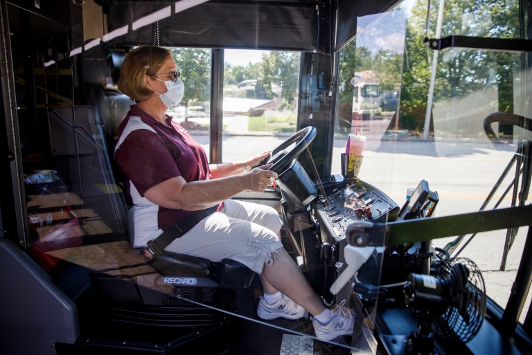 A bus driver wearing a mask seated behind a plexiglass shield