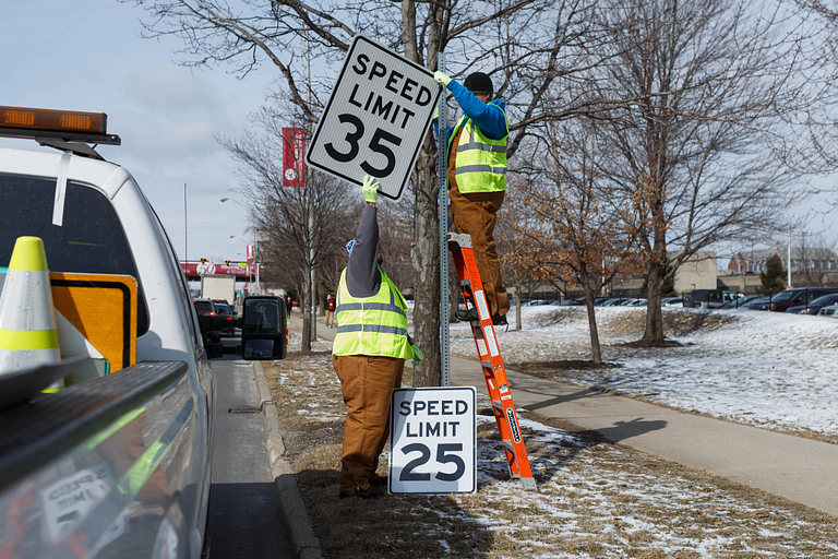 Two city workers change the speed limit signs on Michigan Street.
