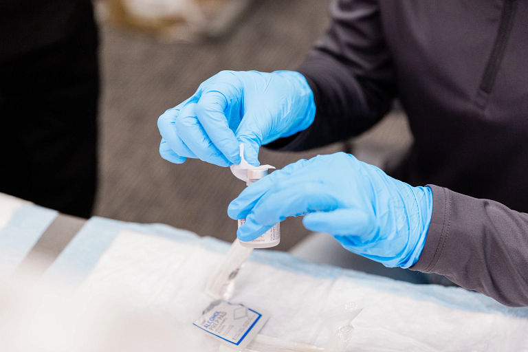 A closeup of gloved hands disinfecting a vaccine bottle