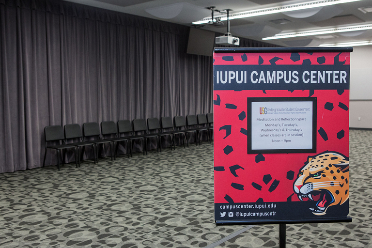 The room is empty, with a line of chairs in the back, and a sign in the foreground, listing hours.