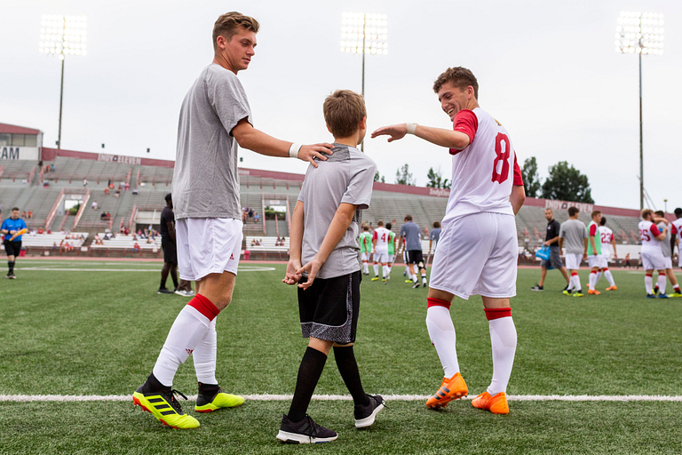 Two soccer players high-five a young boy on the soccer field