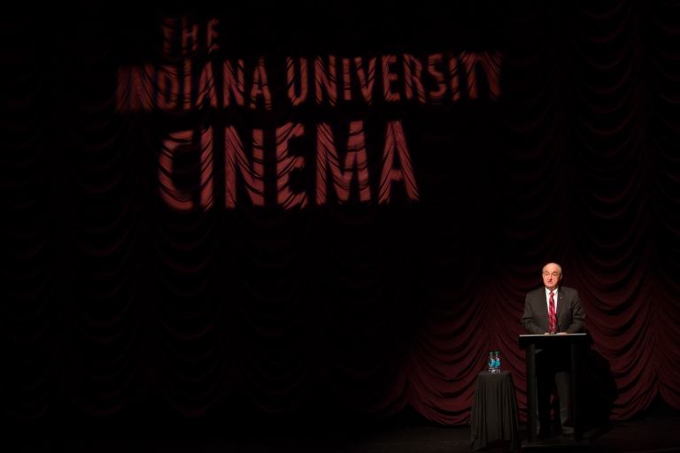 IU President Michael A. McRobbie stands before the curtain on stage at the IU Cinema.