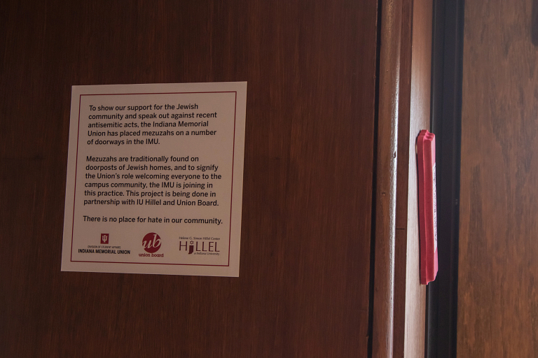 A red mezuzah in a doorway at the IMU with a sign explaining his significance.