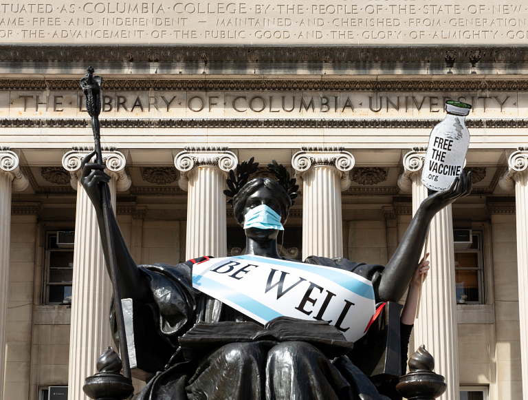 A statue by Columbia University Library wears a mask and a sign that says 'be well'