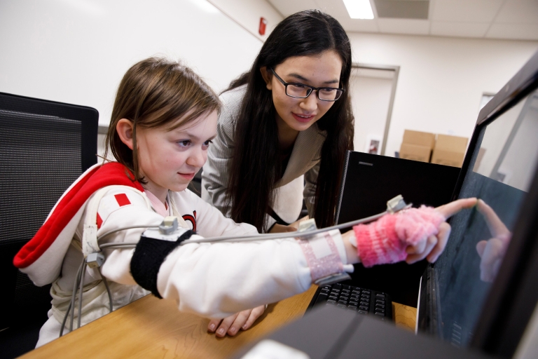 A young girl and a woman point at a computer.